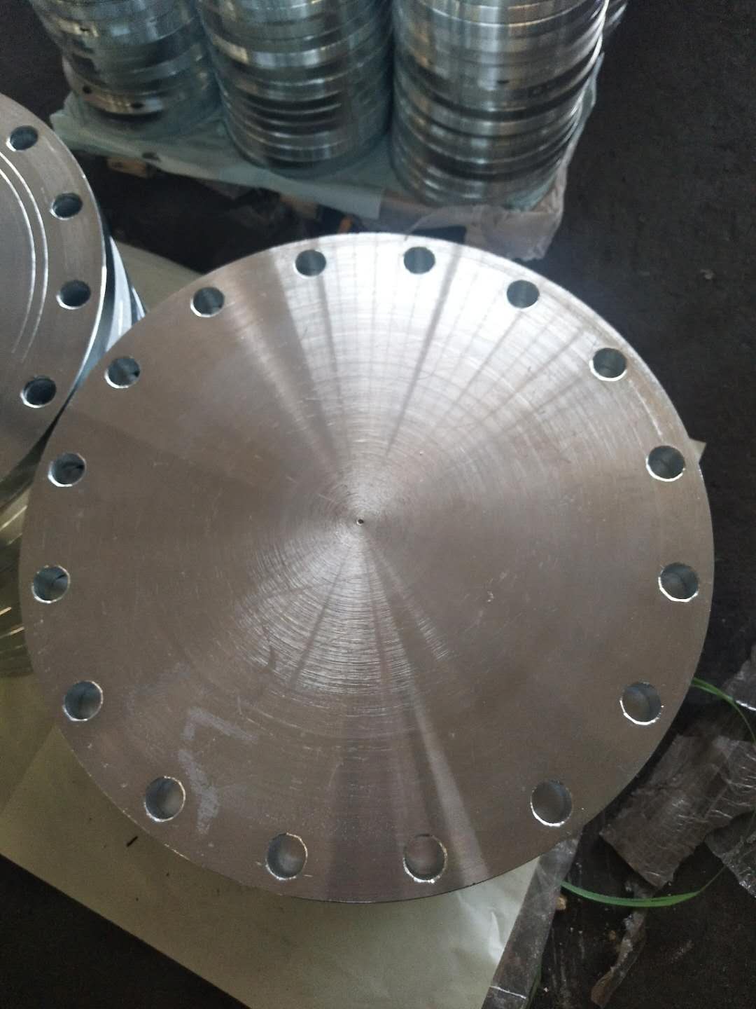 これはステンレス鋼製の大口径ブラインドフランジです。大規模パイプラインシステムの開口端を密閉するために設計された配管部品です。エッジの周囲に均等間隔で複数のボルト穴を備えた堅牢なディスク構造を特徴としており、対応するフランジ（ガスケット付き）にしっかりと固定することで、漏れのない密閉を実現します。