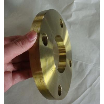 This is a brass plate flange held by a hand, showing its golden metallic surface. It’s a thick circular fitting with a central bore and multiple bolt holes, and has marked size info (like "10×2") on the side. Suitable for corrosion-resistant piping connections in specific industrial scenarios.