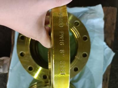 Hand-holding a golden 8" SCH40 PN16 WN flange (marked with specs). Bolt-holed, paired with another flange, on paper (warehouse setting).